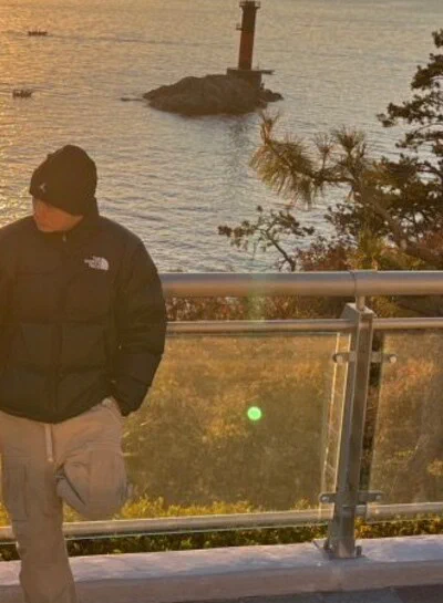 YANGLEE con gorro negro y chaqueta frente al mar